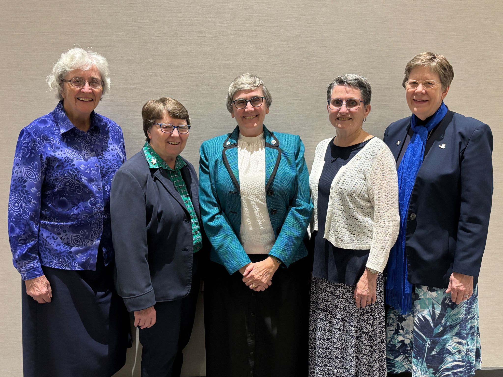 Five women standing in front of a tan wall.